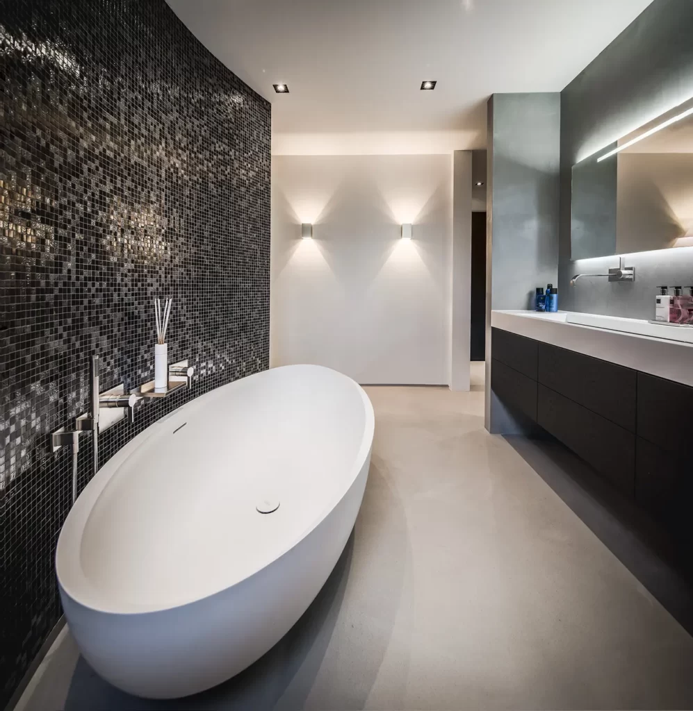 Luxe badkamer met gietvloer en wall-coating in aardse tinten en ronde mozaïek wand om vrijstaand ovalen ligbad