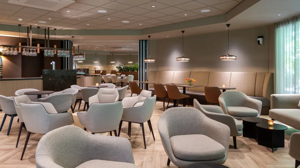 Gezellige zitruimte in Crematorium Venlo met lage ronde tafels, beklede fauteuils en een lange bank tegen de wand.