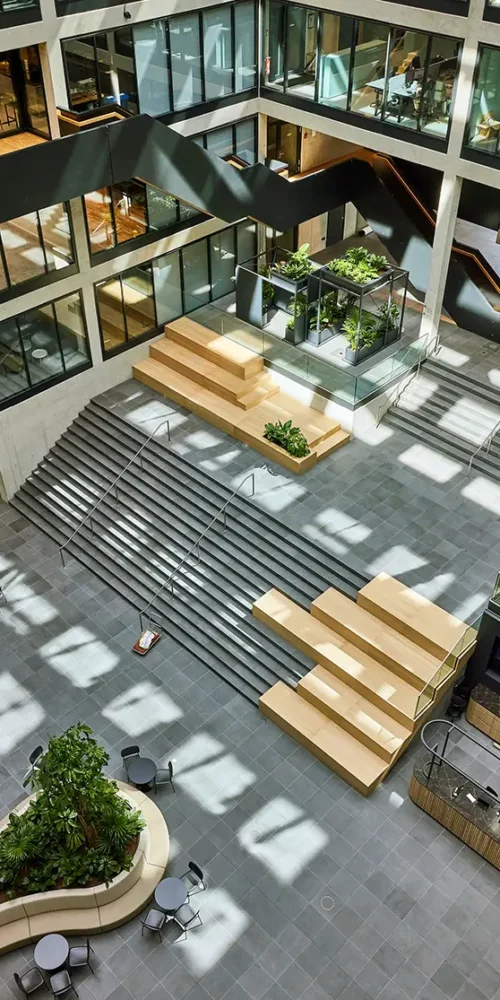 Plamen van Dijk | Design Studio, diagonaal overzicht van een interieurontwerp in een atrium met houten zitelementen op de trap