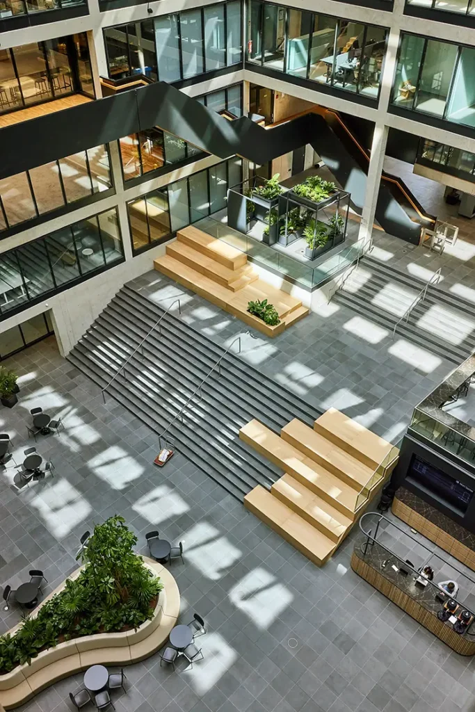 Plamen van Dijk | Design Studio, diagonaal overzicht van een interieurontwerp in een atrium met houten zitelementen op de trap