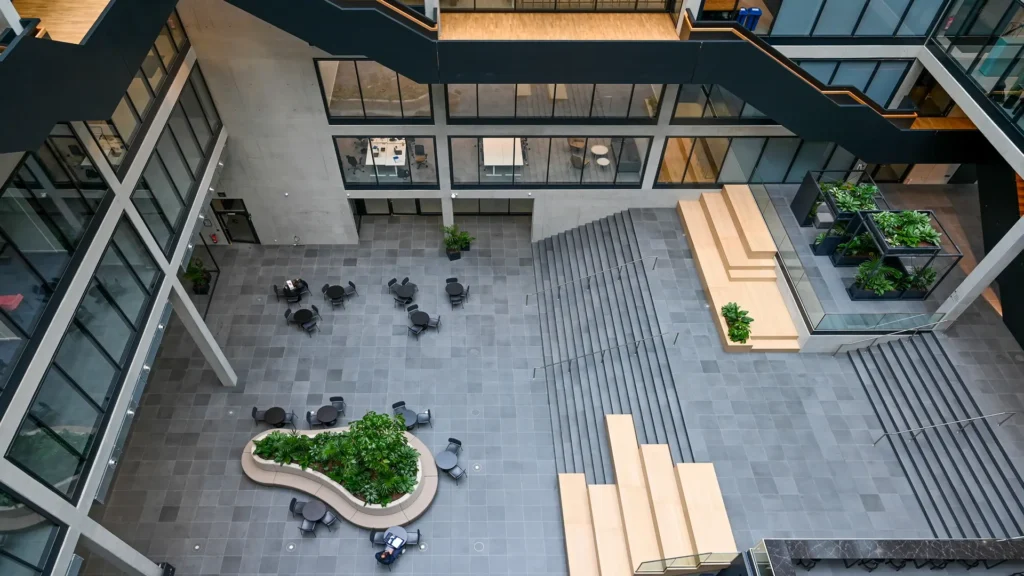 Plamen van Dijk | Design Studio, bovenaanzicht van interieurontwerp van een atrium met houten zitelementen op de trap en organisch gevormde zitbank met plantenbak