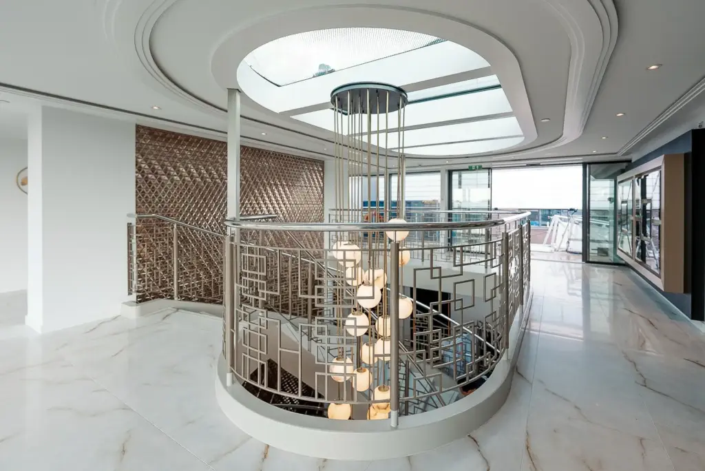 Overzicht van de centrale lobby op het bovenste dek van de Excellence Crown. Het royale daklicht, de open vide, sculpturale verlichting en maatwerkbalustrades verbinden de verschillende niveaus tot één ruimtelijk geheel.